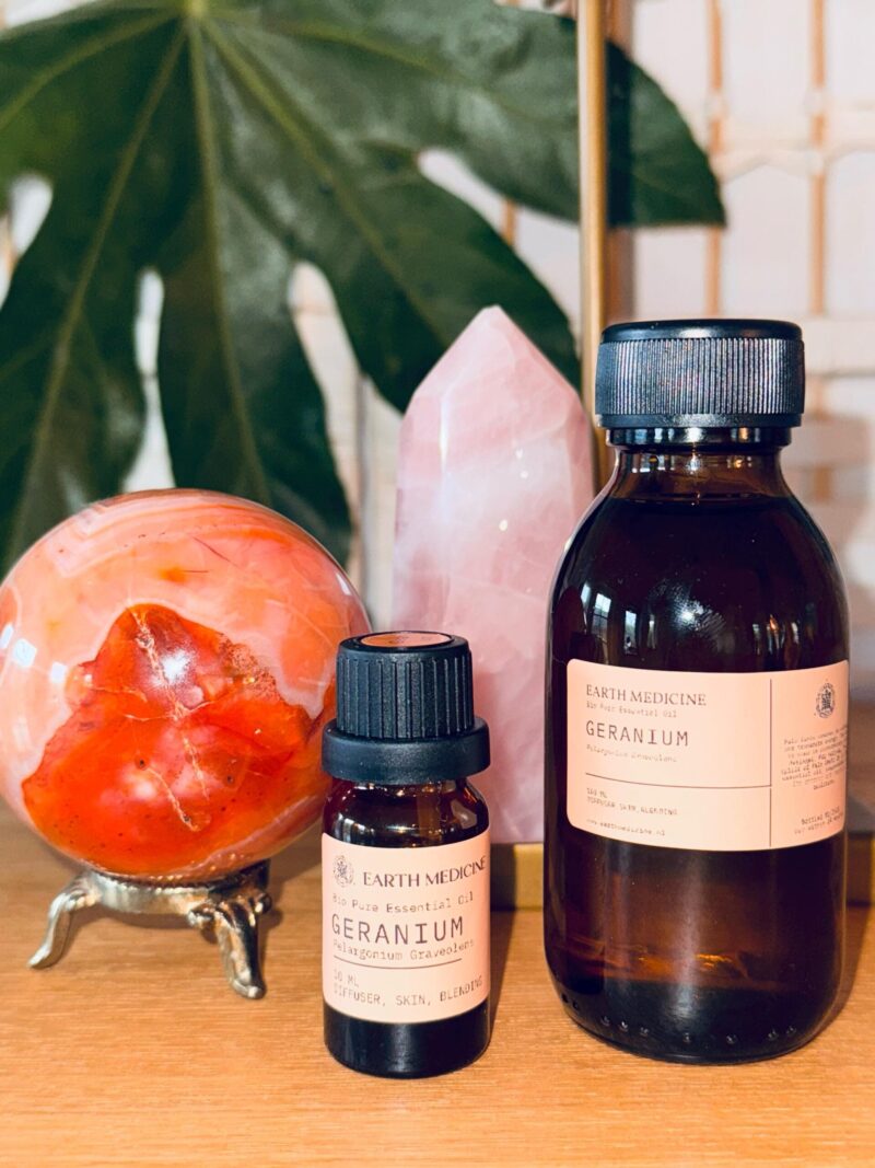 Geraniumolie in 100 ml en 10 ml flesjes met hart- en sacraalchakra kristallen op de achtergrond.
