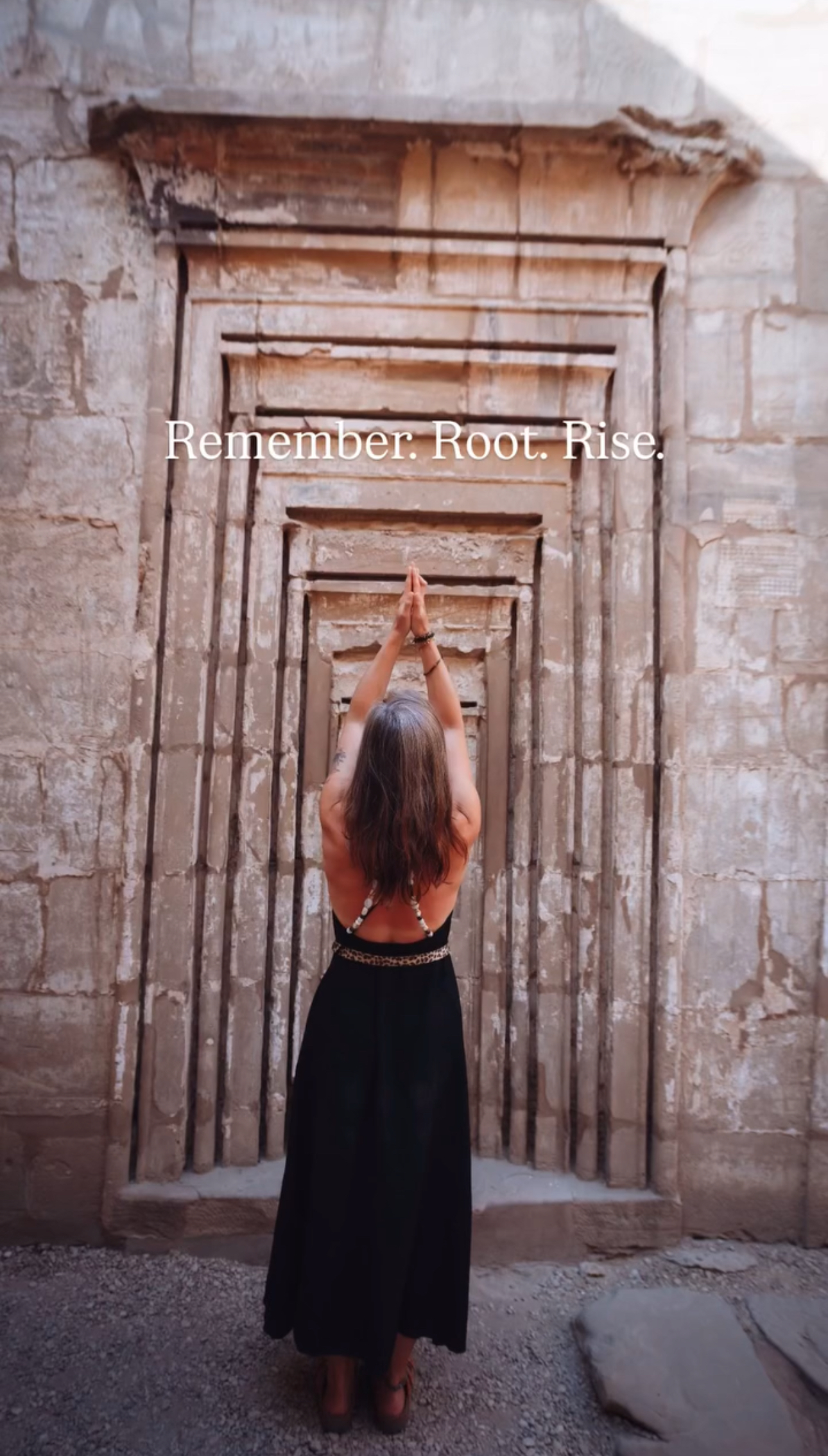 Vrouw met opgestoken armen staat in een tempelopening in Luxor, Egypte, in een rituele houding van overgave en verbinding, met de tekst βRemember. Root. Rise.β erboven.