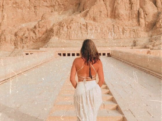 Vrouw loopt de trappen op richting de tempel van Hatshepsut in Egypte, met de tekst ‘Do no harm but take no shit